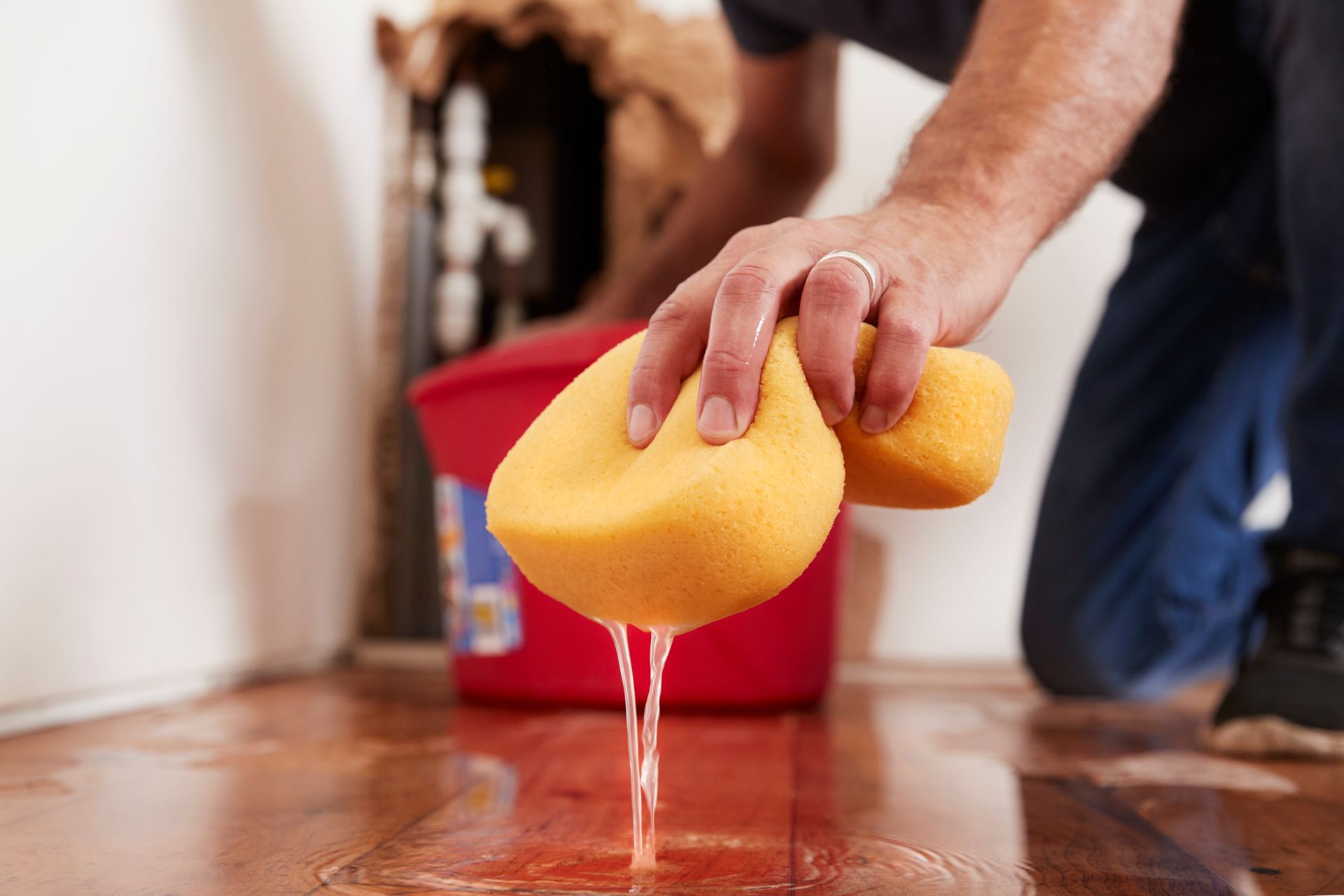 A man is cleaning a flooded floor with a yellow sponge.