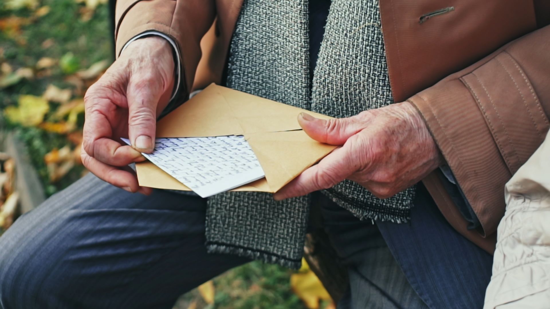 Hands holding a brown envelope with a handwritten note on a bench outdoors