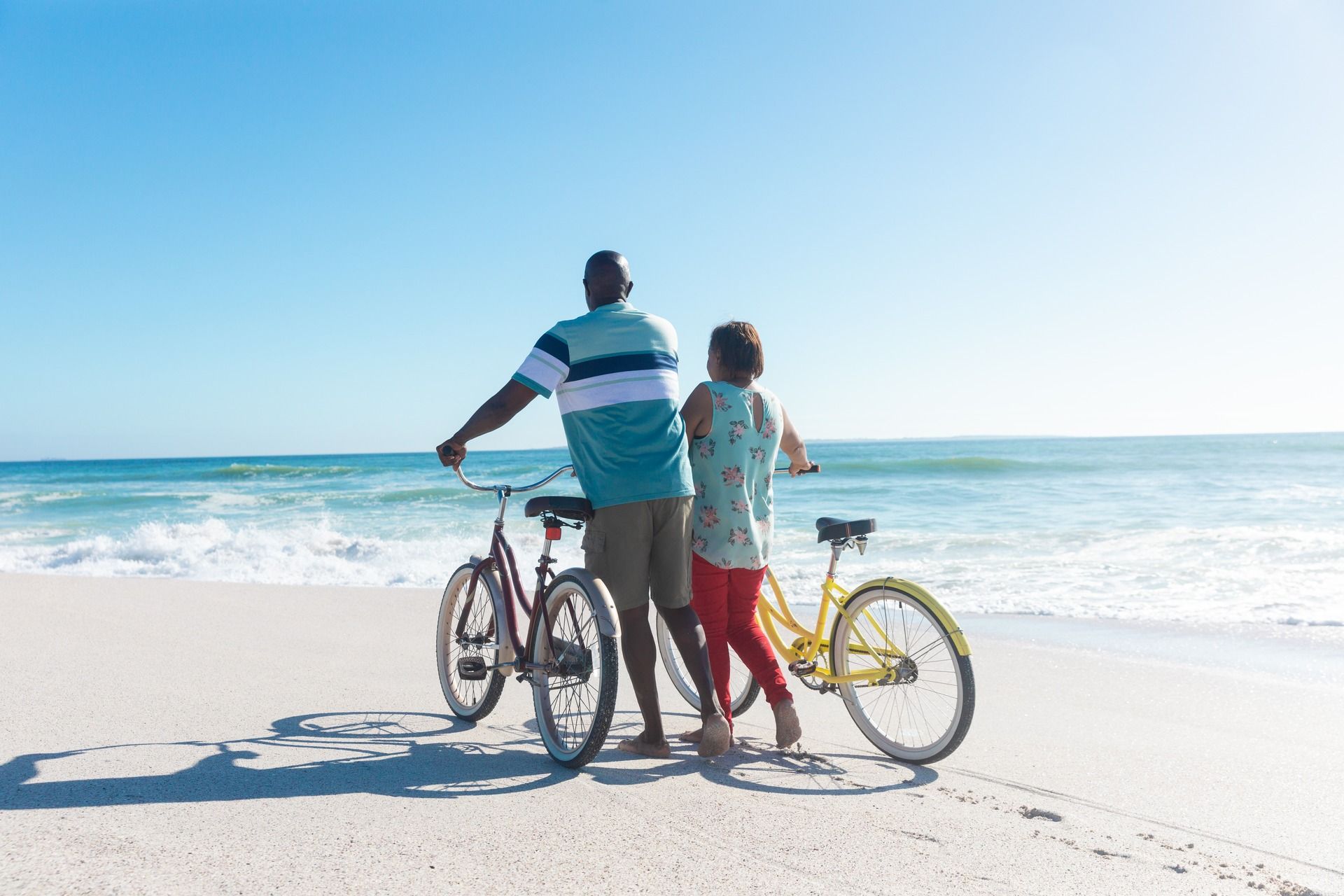 Two people with bicycles on a sunny beach by the ocean