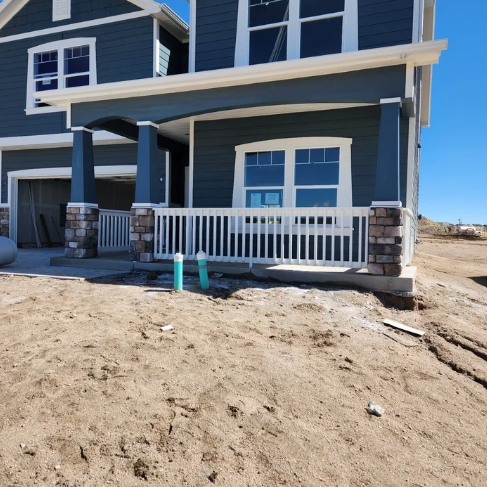 Blue two-story house with a white porch railing on a sandy lot under a clear sky