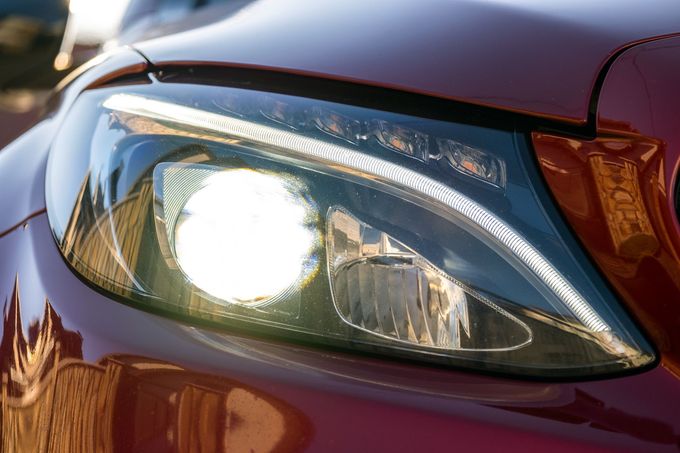 Close-up of a car’s front headlight with bright glare on a maroon hood