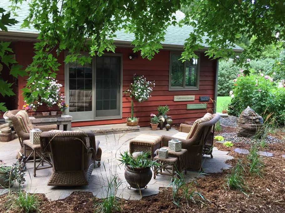 Backyard patio with wooden table and chairs, stone retaining wall, and green lawn behind a house