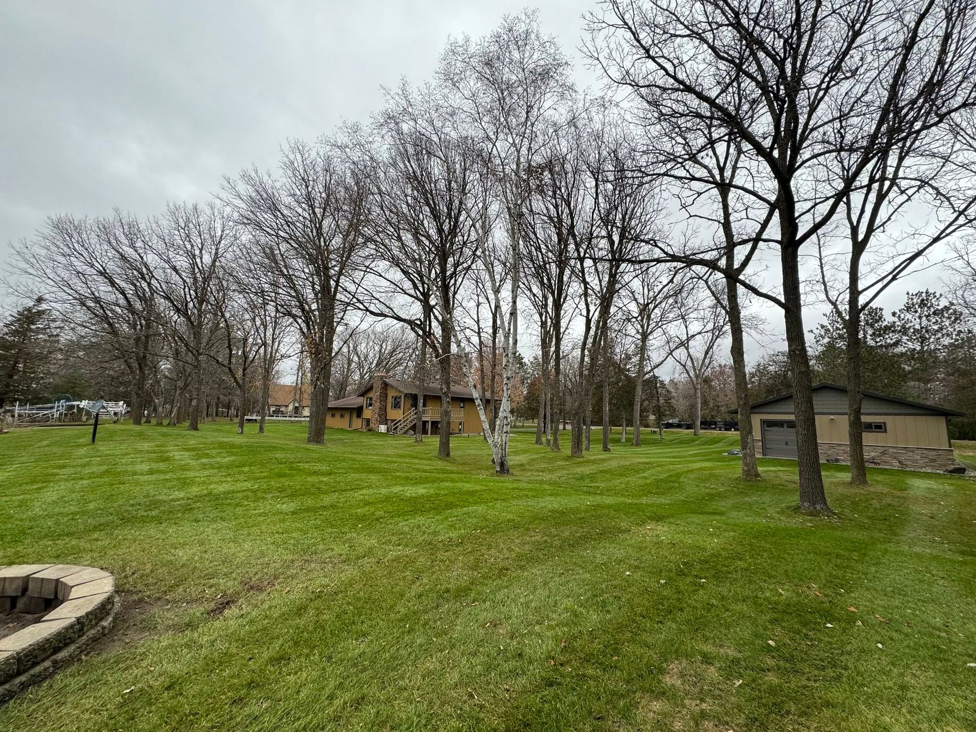 Leafless park with grassy hillside, trees, a pavilion, and a small building under a cloudy sky