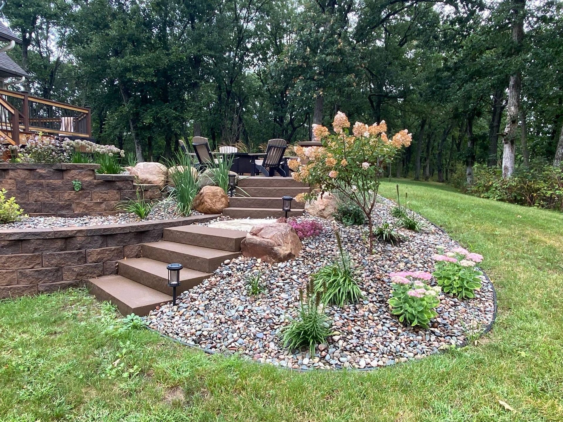 Backyard stone steps and garden bed with flowers, gravel, and green lawn beneath trees