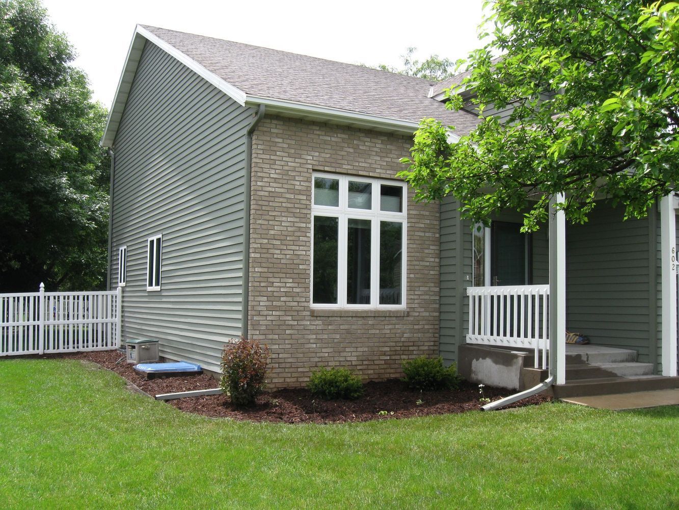 Gray house with white trim, windows, and a small porch, surrounded by green lawn and trees.
