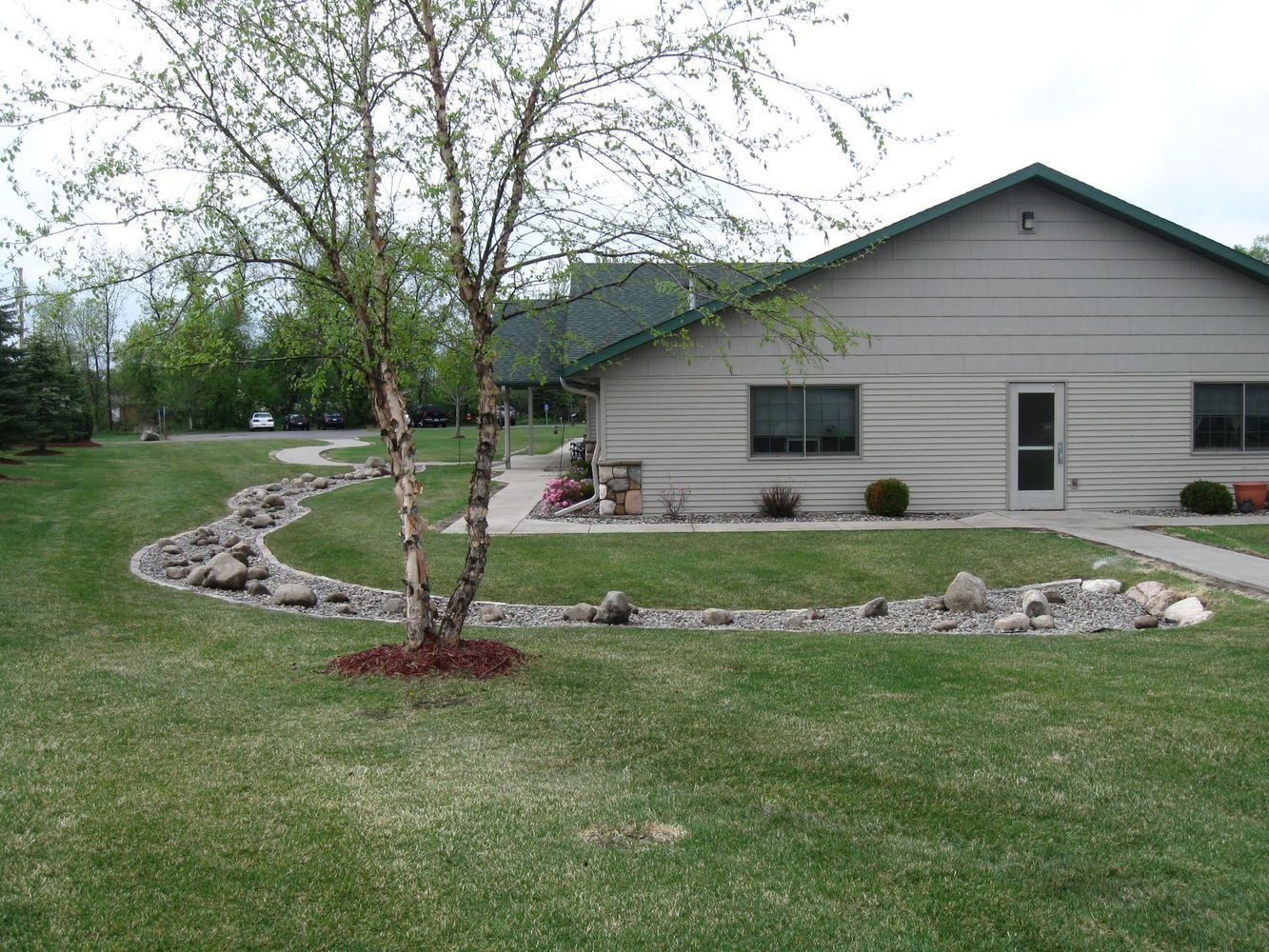 Suburban house with gray siding, landscaped yard, and curved rock border around trees and lawn