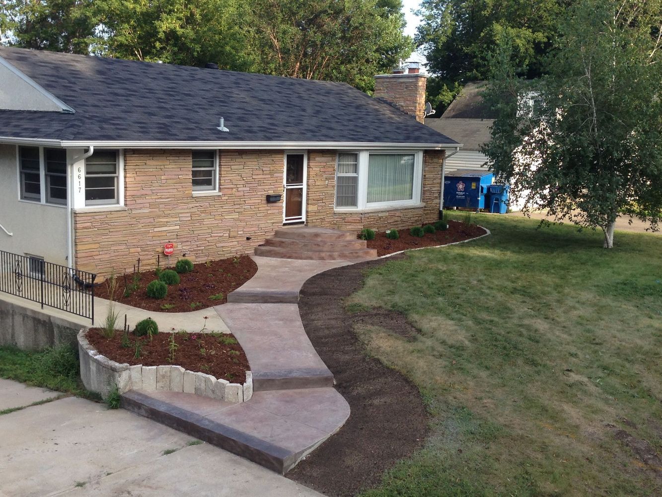 Front yard with a curved concrete walkway leading to a brick house and landscaped garden beds.