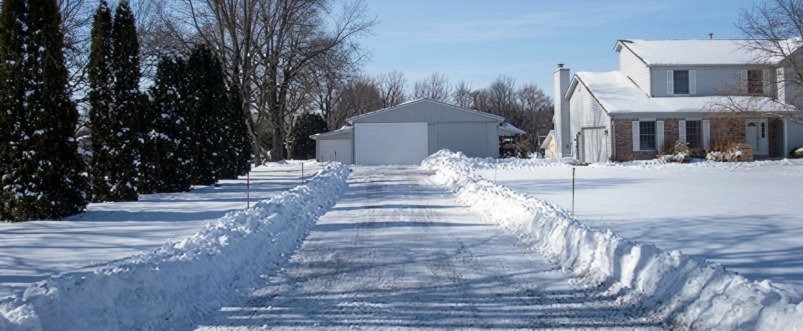 Snow-covered driveway leading to a white house and detached garage on a bright winter day