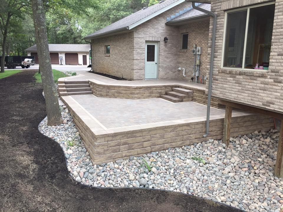 Brick patio and steps beside a house with gravel landscaping and a tree in the yard