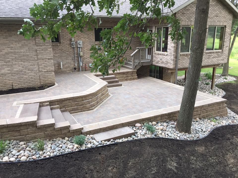 Brick house with a curved stone patio, steps, trees, and a gravel-lined yard.