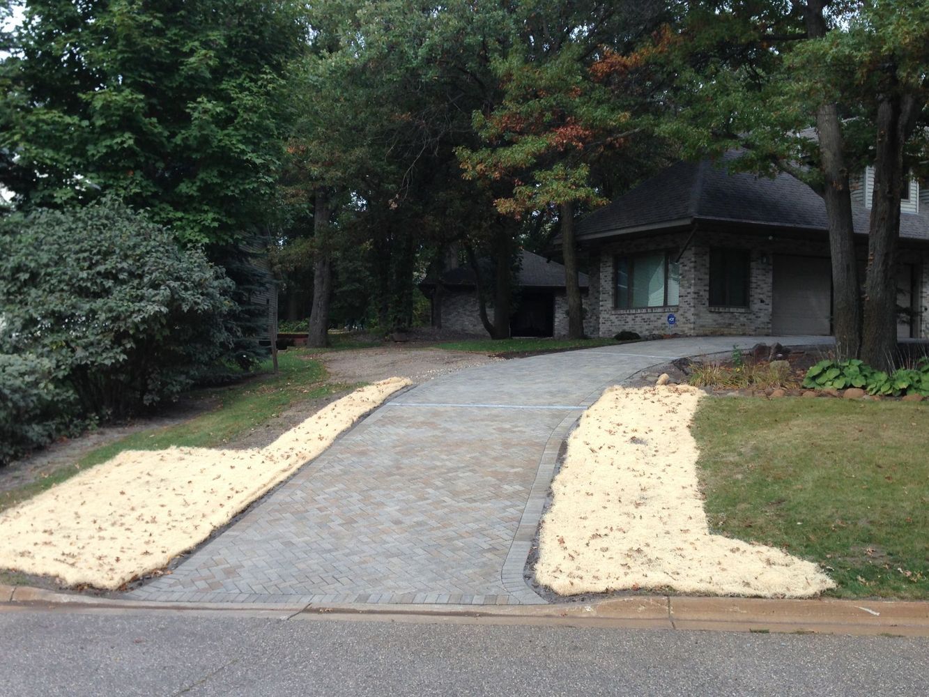 Curved driveway leading to a small stone cottage in a wooded yard, with pale gravel borders.