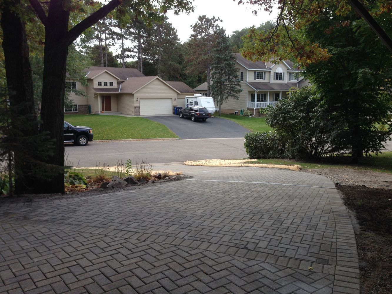 Brick driveway leading to a suburban street with houses and parked cars