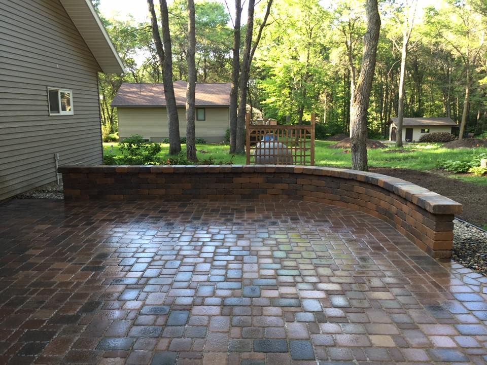Brick patio with a curved retaining wall and wet pavers in a wooded backyard
