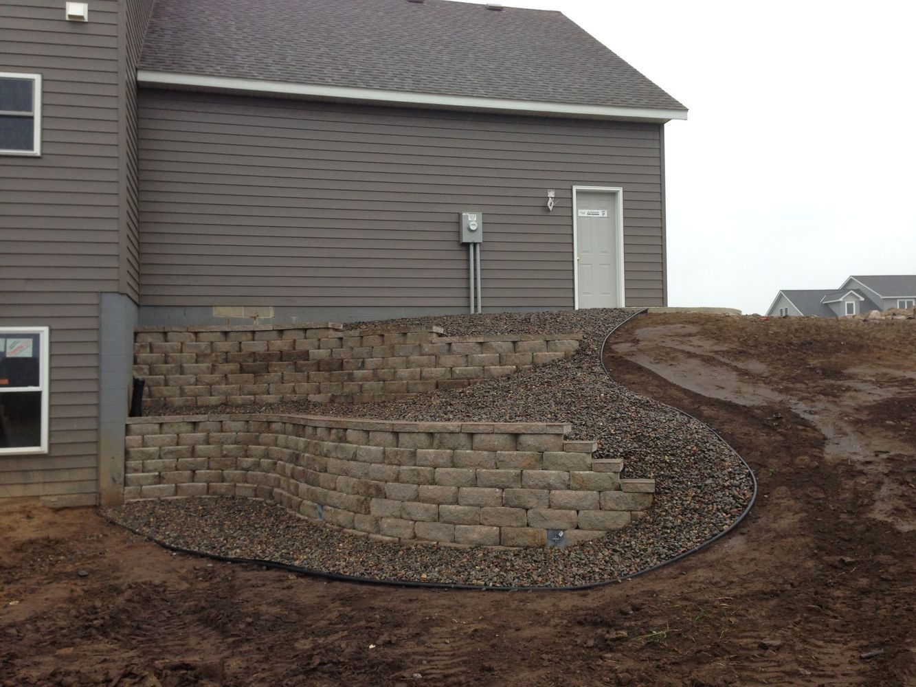 Houseside retaining wall with stacked stone and gravel landscaping on a sloped yard