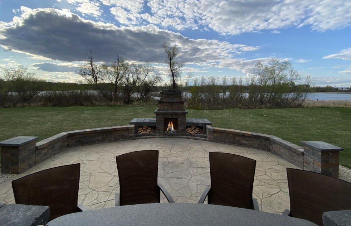 Stone fire pit with curved benches overlooking a lake under a cloudy blue sky