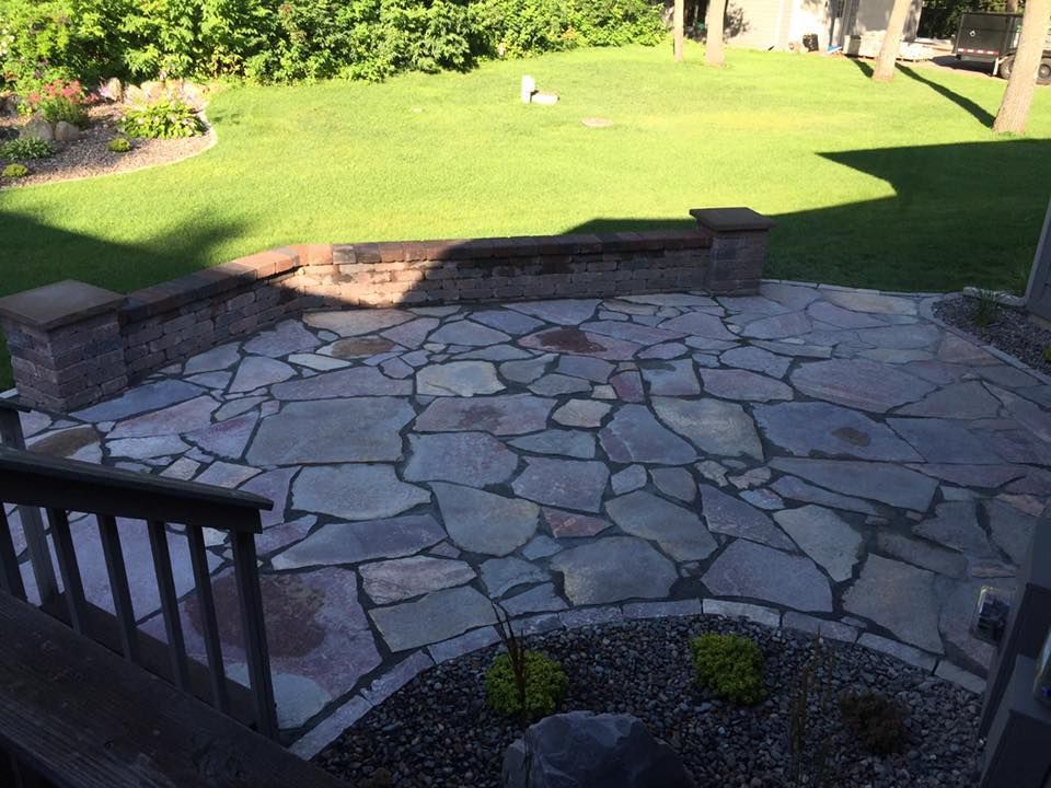 Stone patio steps down to a bright green lawn, with brick retaining walls and garden beds.