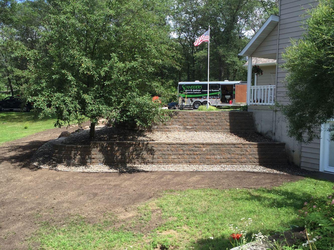 Front yard with terraced steps, trees, and a house porch with an American flag.