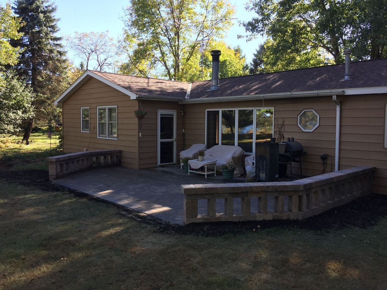 Wooden cabin with a small deck, patio table, and chairs in a wooded yard