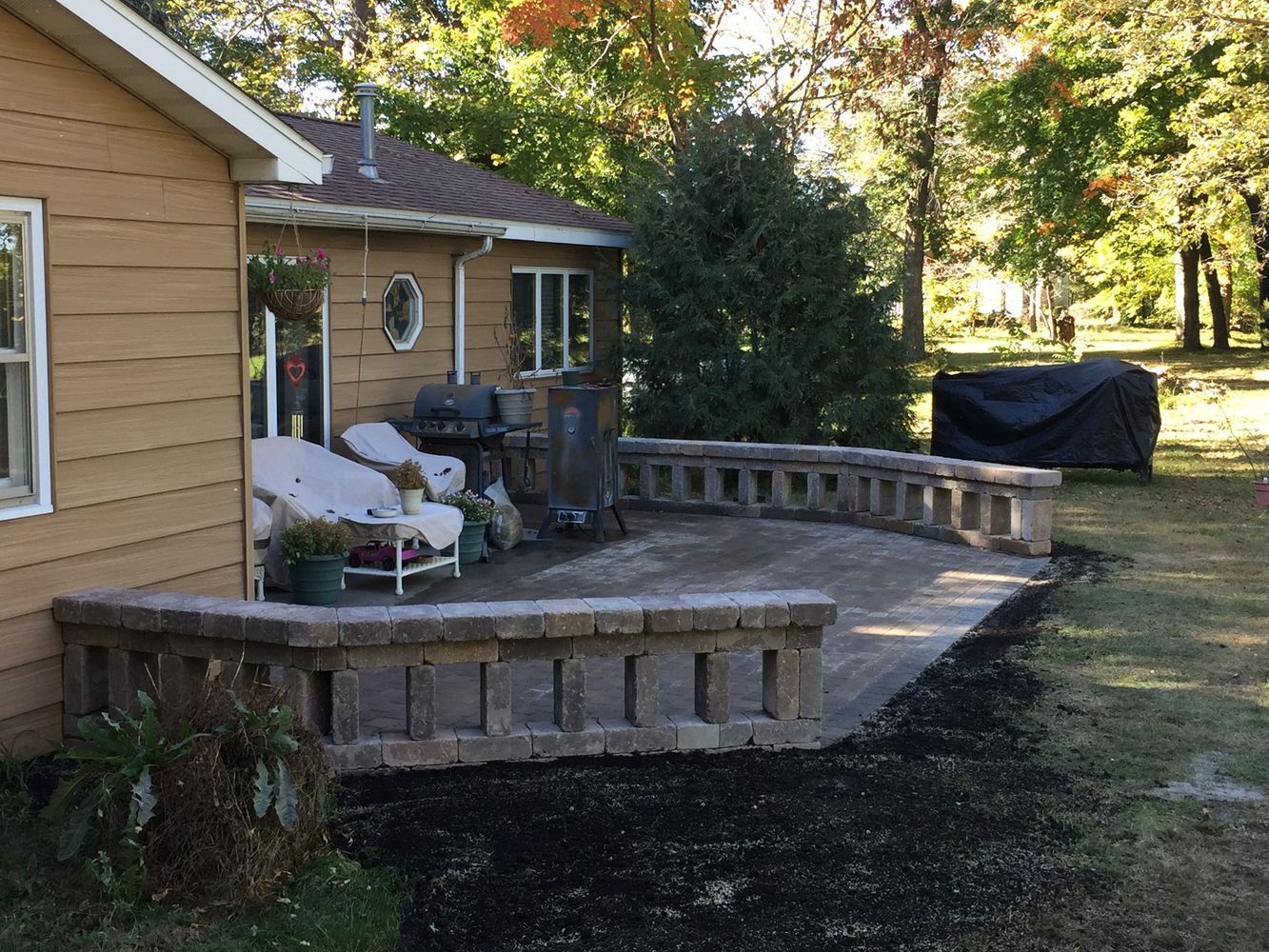 Backyard deck beside a tan house, with chairs, a built-in bench, and a covered grill on the lawn.