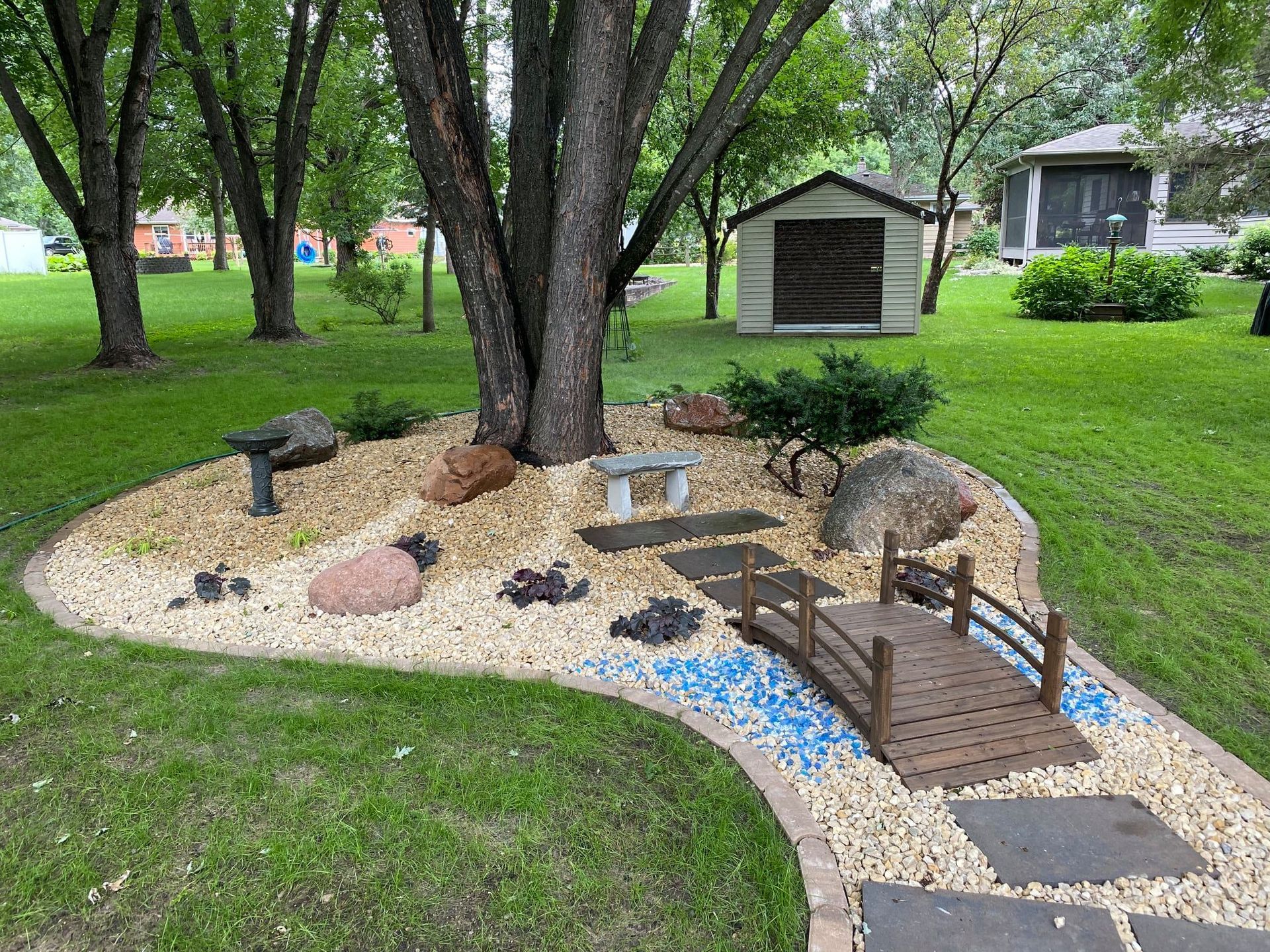 Backyard miniature landscape with trees, a small bridge, pond, and stone path beside a house