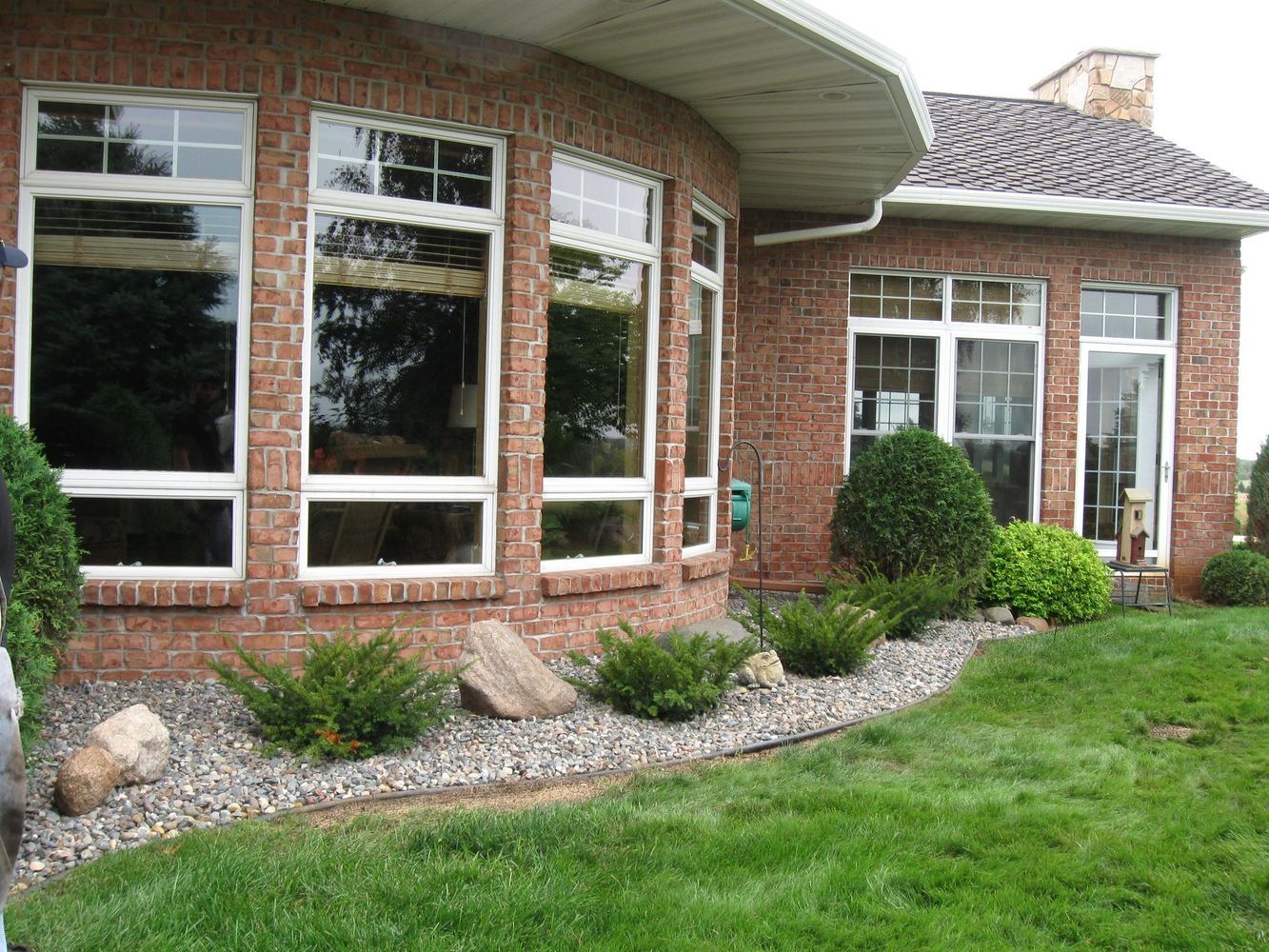 Brick house with curved bay windows, white trim, and a landscaped front yard with rocks and shrubs