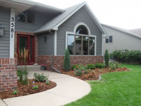 Gray suburban house with red front door, brick porch, curved walkway, and green lawn