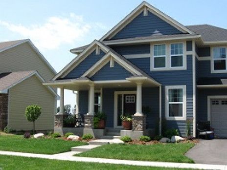 Blue suburban house with white trim, a front porch, and a neatly landscaped lawn