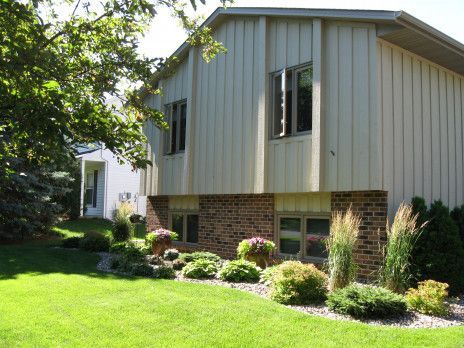 Suburban house with beige siding, brick lower walls, and a landscaped green lawn in front