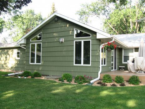 Green house exterior with white trim, front windows, and a small landscaped yard
