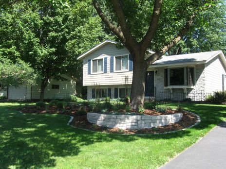 Suburban house with front porch, large trees, and a curved brick-edged lawn bed