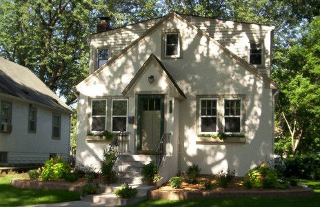 Two-story white house with a green front door, trees, and a small garden in front