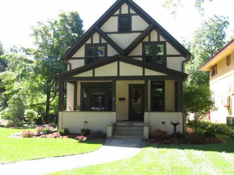 A small Tudor-style house with a gabled roof, cream walls, and dark trim, fronted by a lawn and walkway.