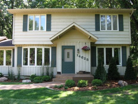 Two-story beige house with green shutters, front porch, and landscaped yard