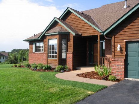Suburban brick house with green lawn, curved walkway, and driveway under a partly cloudy sky