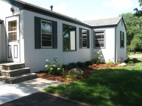 White house exterior with dark trim, front steps, and landscaped lawn in sunlight
