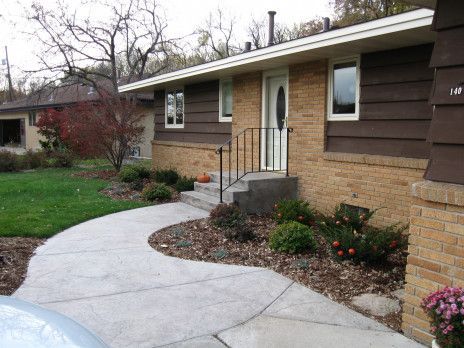 Front entrance of a house with a curved concrete walkway, brick steps, and landscaped flower beds