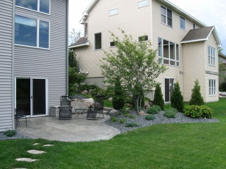 Backyard patio beside beige apartment buildings with green lawn, shrubs, and outdoor seating