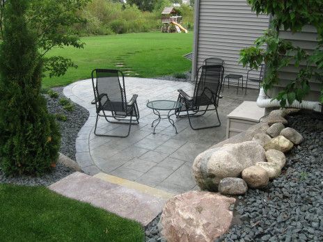 Patio with two black chairs, stone paving, and landscaped rocks beside a house