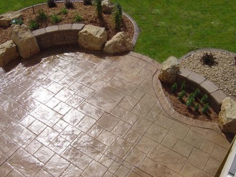 Paved patio with stamped concrete and curved stone planter walls around landscaped garden beds.