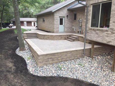 Brick house patio with raised concrete deck, steps, and gravel landscaping along the side yard