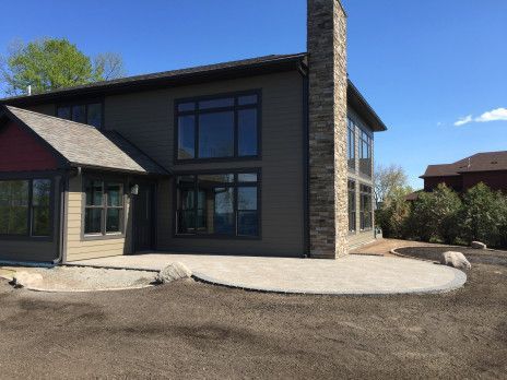 Modern two-story house with stone chimney, dark siding, and large windows in a sunny yard