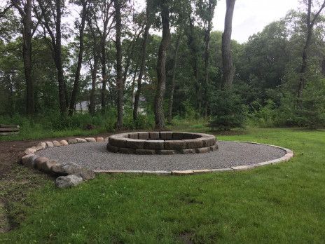 Circular stone fire pit in a grassy park with trees in the background