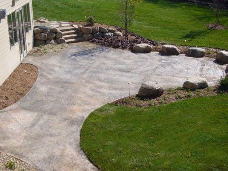 Gravel driveway beside a house, bordered by grass and large decorative rocks.