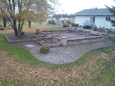 Backyard stone patio and terraced garden with trees beside a white house in autumn