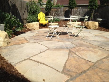 Patio with large stone paving, white table and chairs, yellow Adirondack chair, and garden border