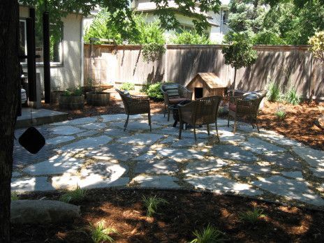 Patio with stone pavers, outdoor dining table and chairs, wooden fence, and trees in a shaded backyard