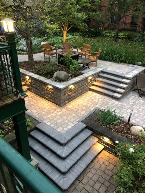 Terraced garden patio with stone steps, potted plants, and outdoor chairs lit by warm lights