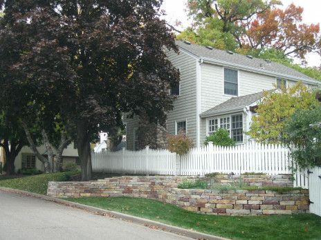 White house with picket fence and stone retaining wall beside a tree-lined street