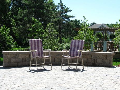 Two striped patio chairs on a stone patio with a low wall and trees in the background