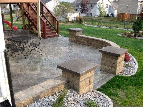 Stone patio with steps, railing, and round table beside a grassy backyard.